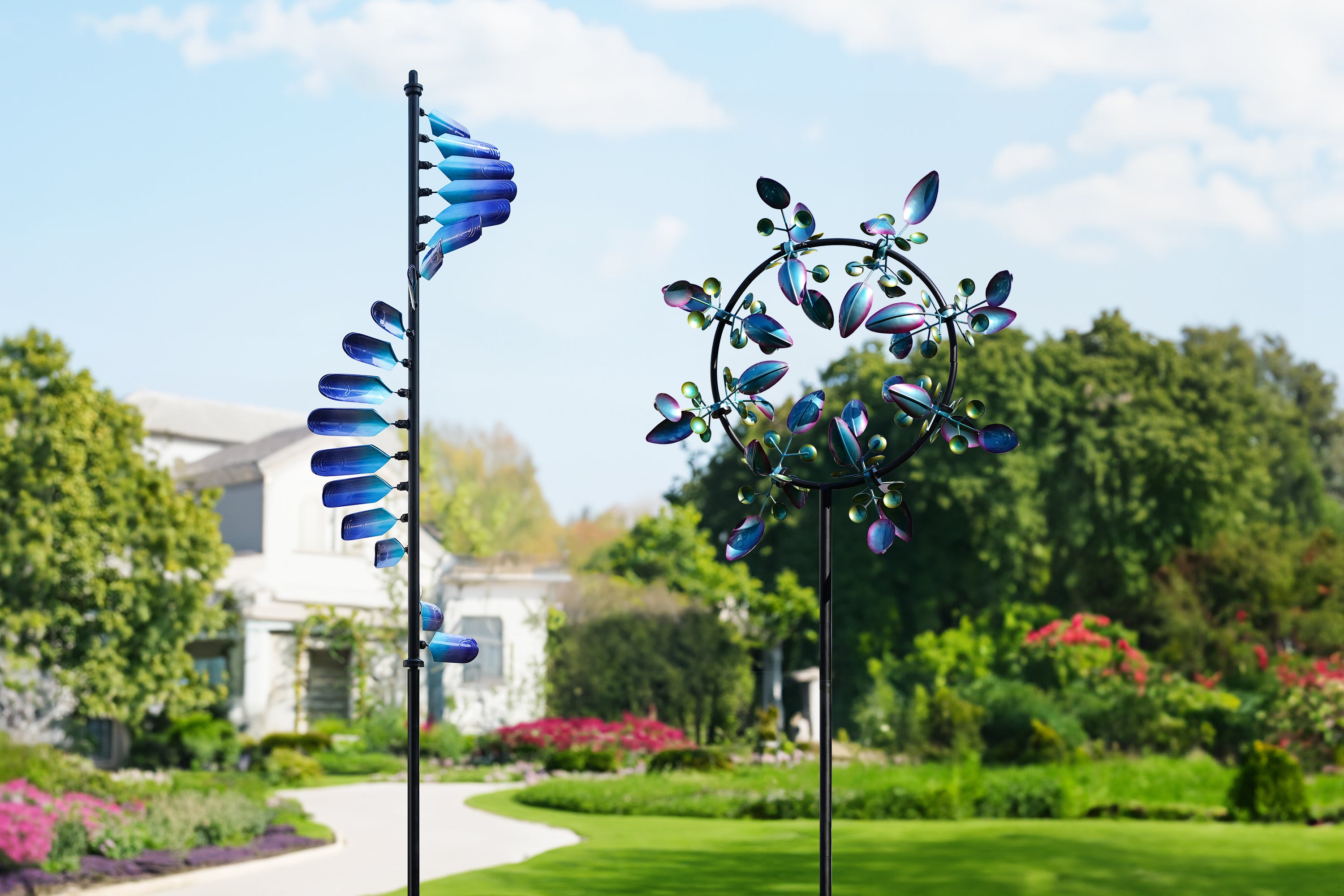 This image shows two windmills set in a lush garden. The left windmill's blades are arranged in a spiral, and the gradient of blue adds a sense of movement. The right windmill is round and brightly colored, with blades resembling blooming flowers. In the background, the white buildings and colorful flower beds complement the windmills, creating a tranquil and beautiful atmosphere.
