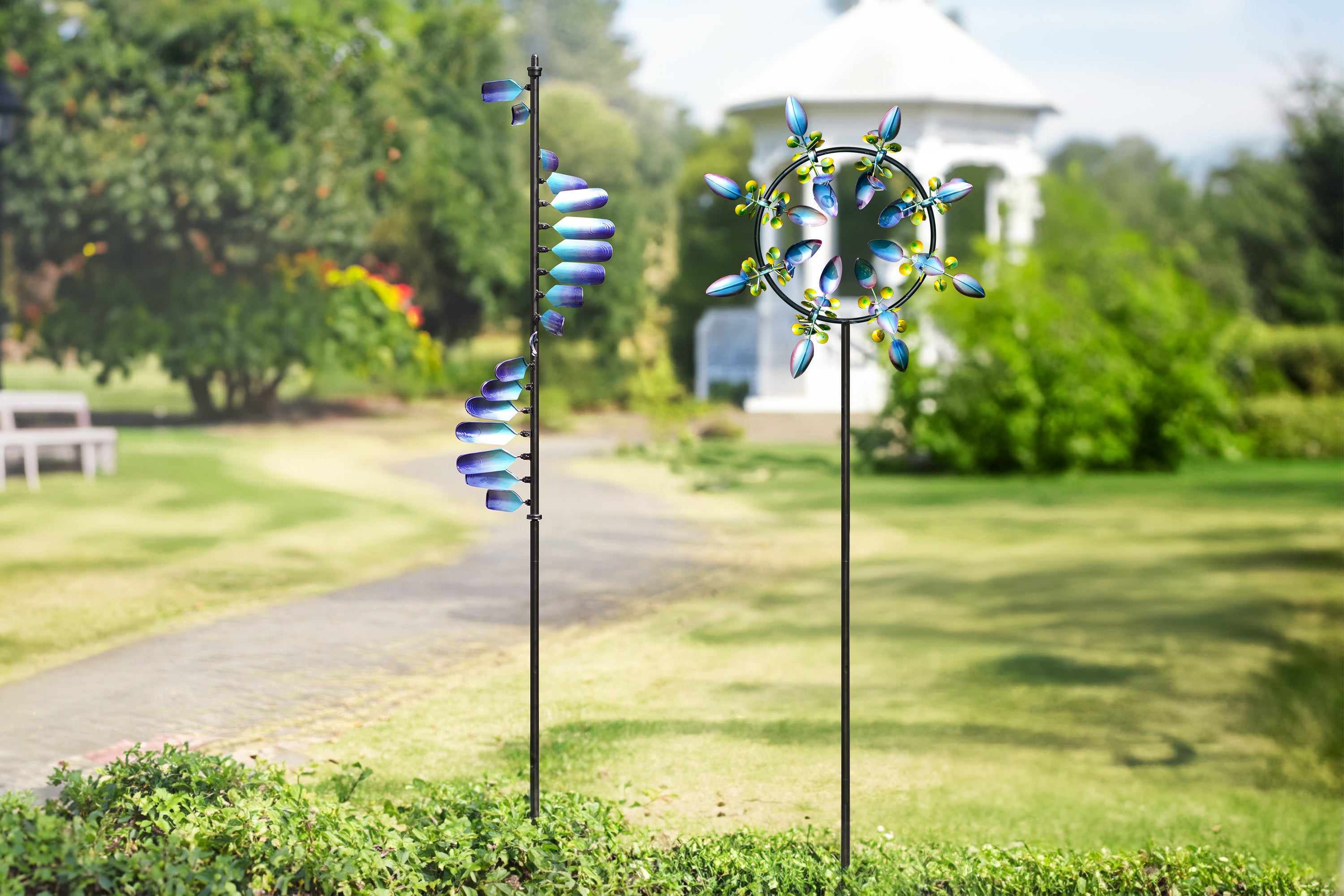 This image shows two windmills, each standing beside a beautiful garden path. The left windmill's spiral blades, with a blue gradient design, create a dynamic effect. The right windmill, with its circular structure and evenly spaced, colorful blades, resembles a blooming flower. In the background, a white pavilion and surrounding greenery create a tranquil and pleasant scene.