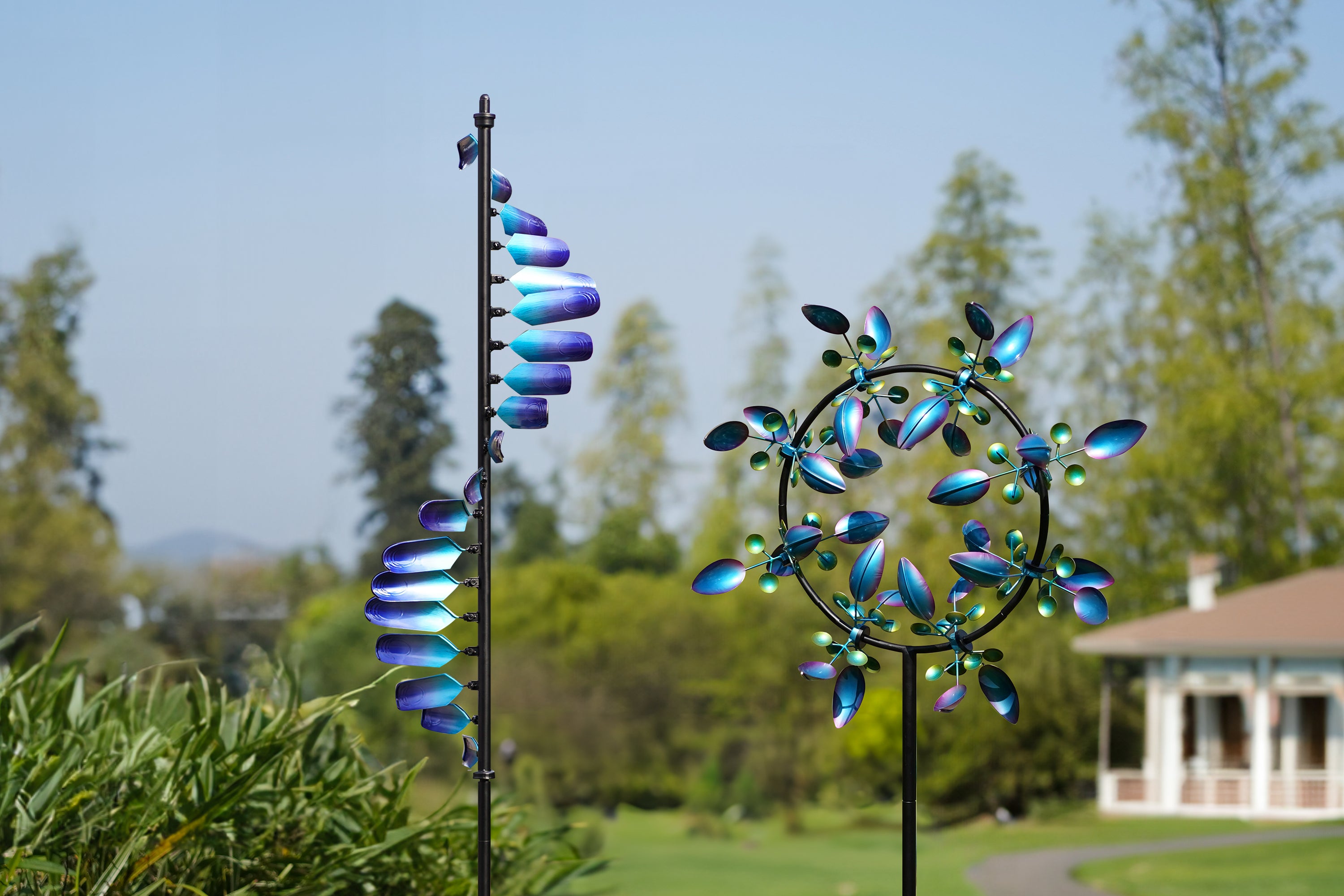 This image shows two brightly colored windmills, each in a different design, adorning a vast meadow. The windmill on the left, with its vertically arranged blades in a gradient blue, presents a simple and modern form. The windmill on the right, with its rounded shape and evenly spaced blades and vibrant colors, resembles a blooming flower. The houses and greenery in the background add a tranquil atmosphere to the scene, while the windmills' gentle rotation in the breeze adds a sense of dynamism and vitality